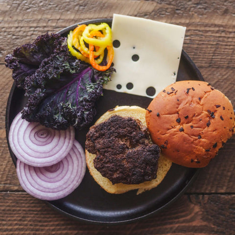 Black skillet with Wagyu Ancestral ground beef burger ingredients on a wooden surface